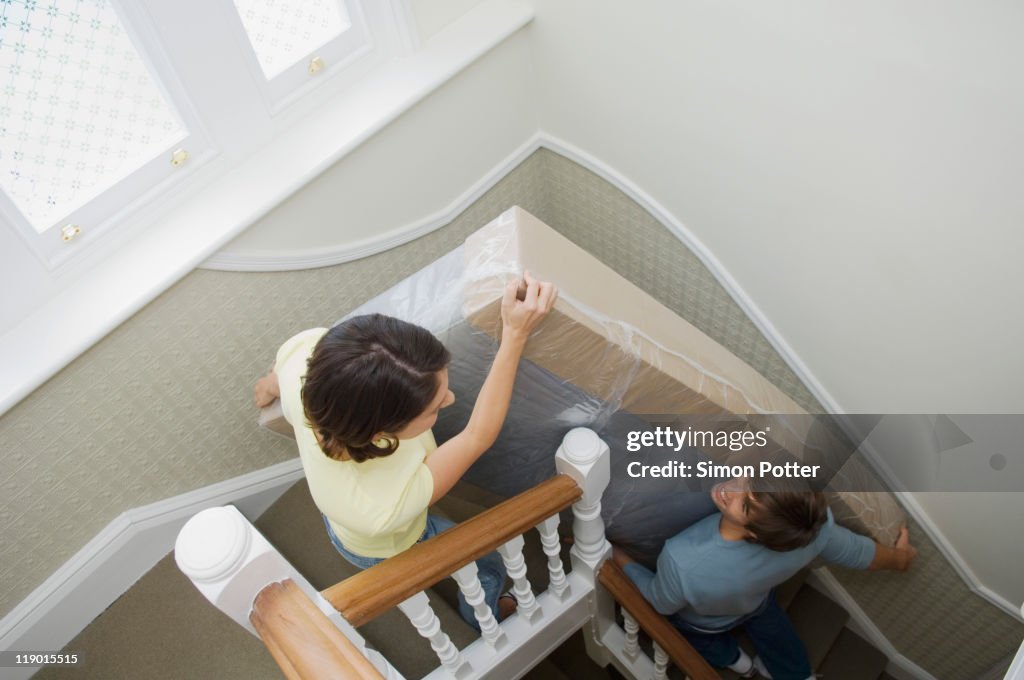 Couple carrying mattress upstairs