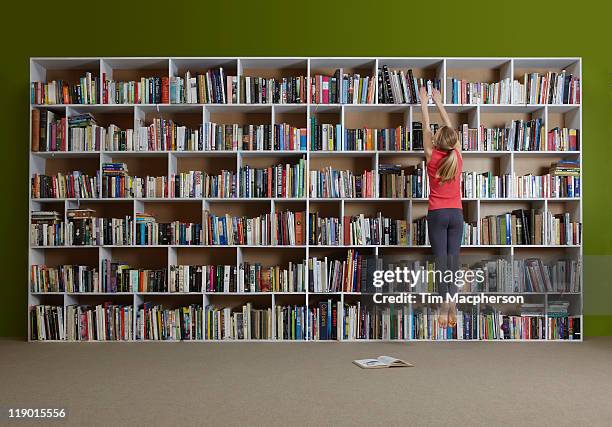 girl jumping for book on high shelf - bookshelf stock pictures, royalty-free photos & images