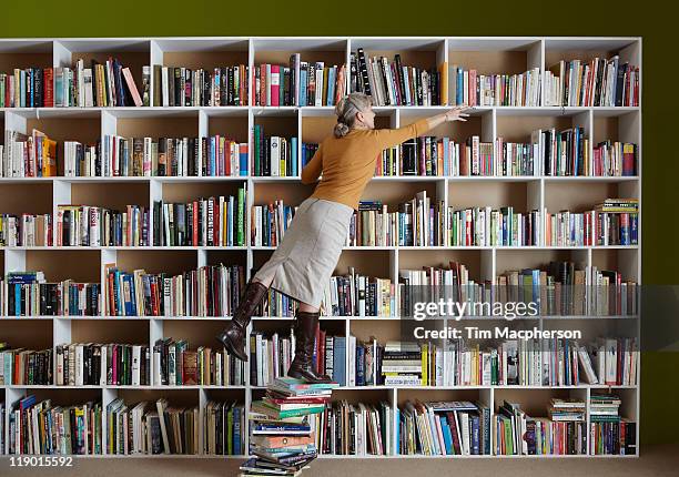 older woman standing on stack of books - woman reaching stock pictures, royalty-free photos & images