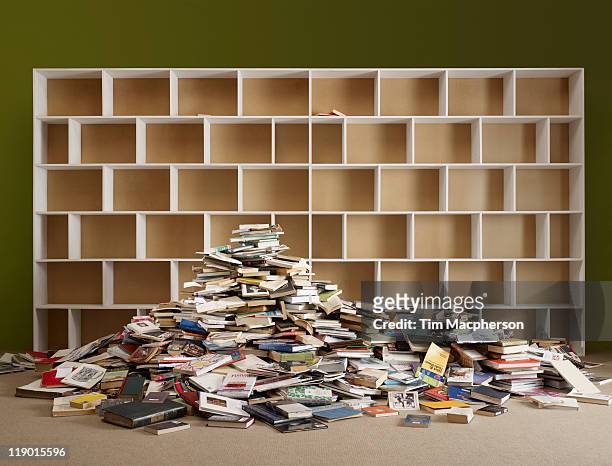 pile of books by empty shelves - library empty stock pictures, royalty-free photos & images