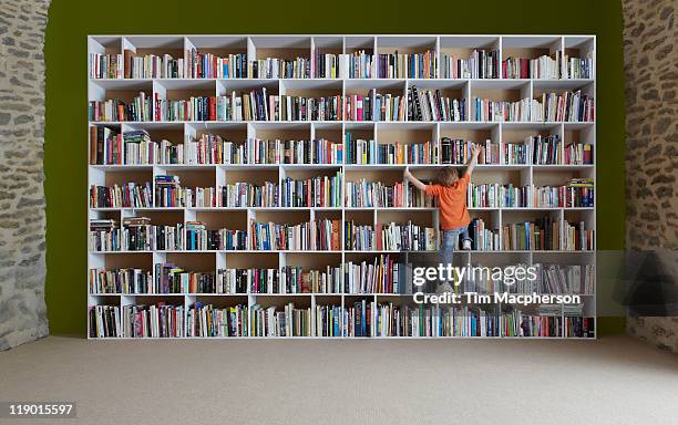 boy climbing bookshelves - bookshelf foto e immagini stock