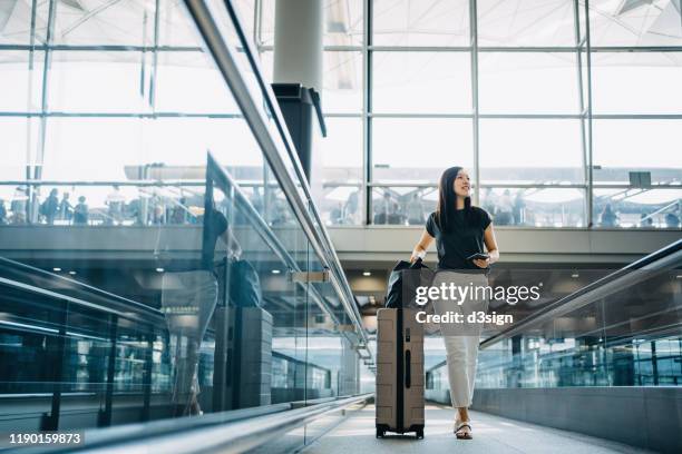 young asian woman with passport carrying suitcase walking in the airport concourse - travellers stock-fotos und bilder