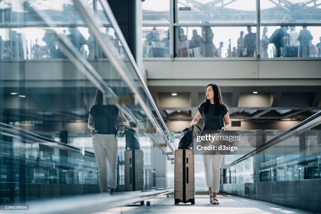 Young Asian woman with passport carrying suitcase walking in the airport concourse