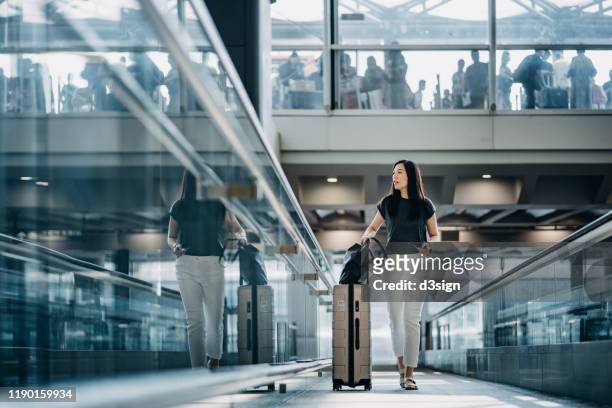 young asian woman with passport carrying suitcase walking in the airport concourse - airport departure area stock pictures, royalty-free photos & images