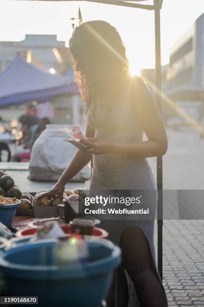 african girl standing in a market holding a smartphone - webfluential - fotografias e filmes do acervo