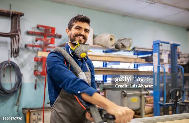 smiling carpenter using grinder in workshop - vorderasiatische abstammung stock-fotos und bilder