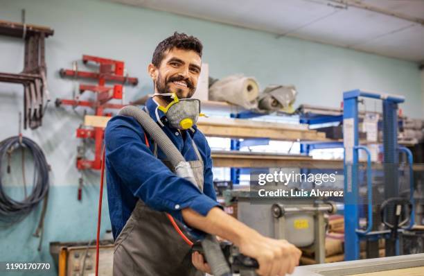 smiling carpenter using grinder in workshop - blue collar worker mask stock pictures, royalty-free photos & images