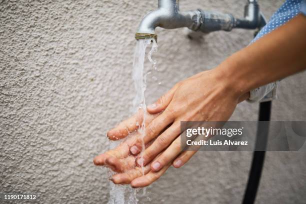 woman washing hands under faucet against wall - parte de fotografías e imágenes de stock