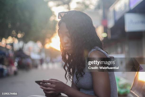 african girl standing in a market holding a smartphone - webfluential - fotografias e filmes do acervo