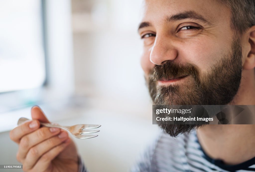 Close-up of mature man indoors at home, eating cake.