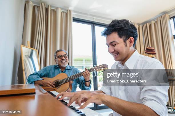 asian adult son enjoy playing piano and senior father playing guitar together in living room at home - asian and indian ethnicities imagens e fotografias de stock