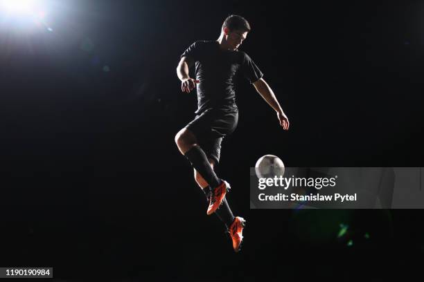 football player jumping with ball on dark background - soccer boot stock pictures, royalty-free photos & images