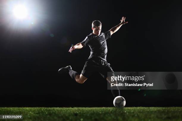 soccer player kicking ball on grass, dark background - studded footwear stock pictures, royalty-free photos & images