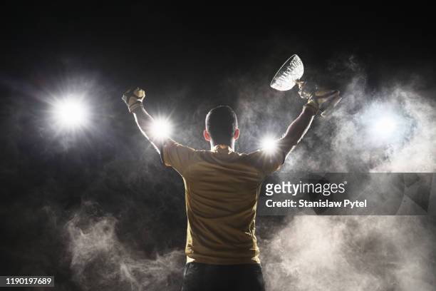 soccer player holding crystal cup and celebrating victory on smoky background - winning stock pictures, royalty-free photos & images