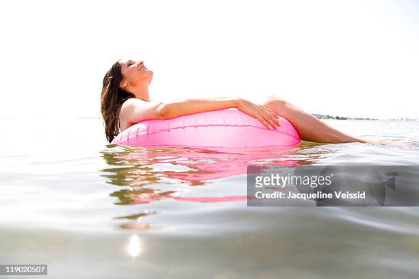 woman floating on pink inner tube on water - standing water stock pictures, royalty-free photos & images