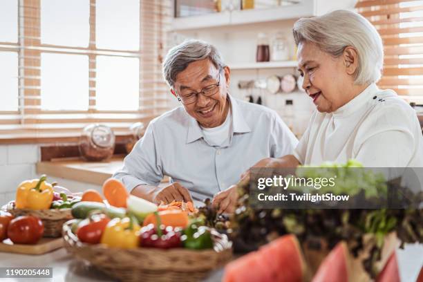 senior asian couple cooking together in kitchen - seniors healthy lifestyle stock pictures, royalty-free photos & images