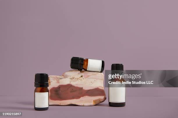 three small brown bottles with white labels sit on a rhodonite stone with a pink background - brown bottle stock pictures, royalty-free photos & images