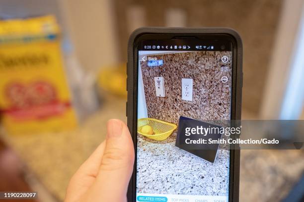 Hand of a man holding a smart phone and using Augmented Reality features in the Amazon shopping app to visualize an Amazon Echo Show device on a...