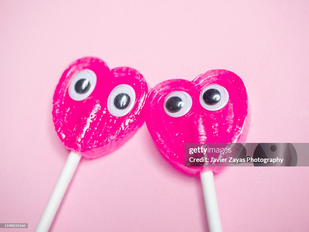 Two Pink Heart Lollipops With Eyes In Pink Background