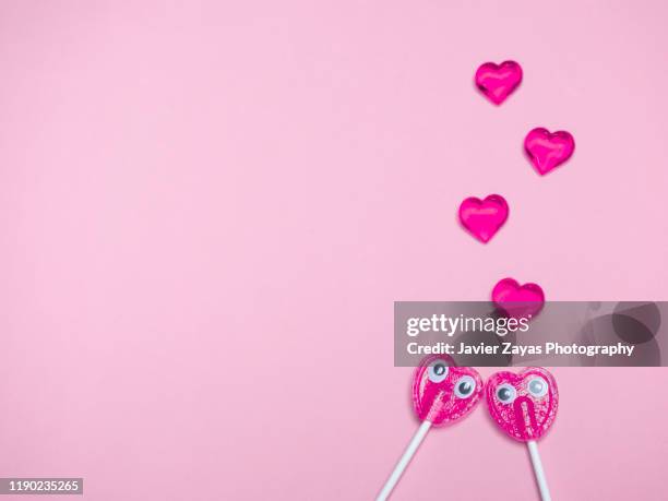 two pink heart lollipops with eyes falling in love in pink background - love at first sight stock-fotos und bilder