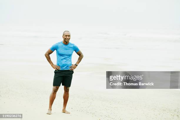 mature man resting after early morning run on beach - black shorts stockfoto's en -beelden