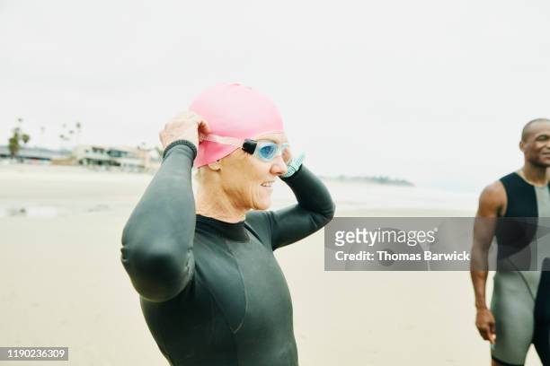 mature woman adjusting goggles before early morning open water swim with friends - california strong stockfoto's en -beelden