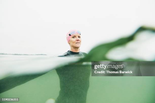 portrait of mature woman treading water during open water swim in ocean - open workouts stock-fotos und bilder