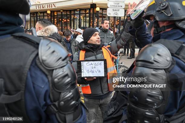 Man holds a box for strike fund donation in front of CRS riot policemen during a demonstration of railway workers on December 23, 2019 outside the...