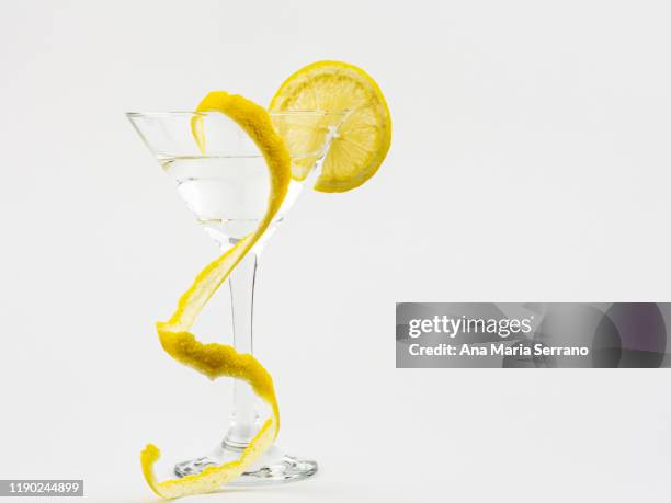 cocktail in a triangular glass cup with a slice of lemon and lemon peel on a white background cutout - lemon peel stock pictures, royalty-free photos & images