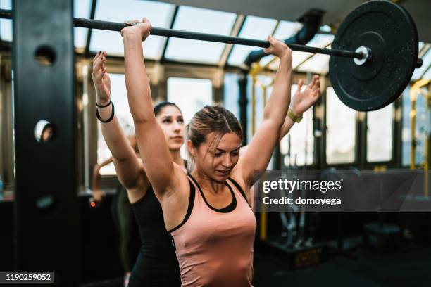 dos mujeres jóvenes levantando pesas en el gimnasio - entrenador personal fotografías e imágenes de stock