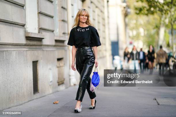 Jeanette Madsen wears earrings, a black Alessandra Rich t-shirt, shiny black crocodile pattern high waist leather pants, a blue fringy bag, black...