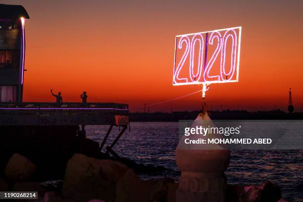 Palestinian youths pose for a "selfie picture" by the Mediterranean sea waterfront in Gaza City on December 23 a with a neon sign reading "2020" in...