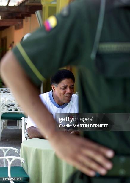 Head coach of the Colombian soccer team, Francisco Maturana, eats his breakfast as a soldier stands guard, 18 July 2001 in Barranquilla, Colombia....