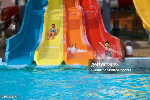 three girls having fun sliding in a waterpark, rainbow colors. - child slide stockfoto's en -beelden
