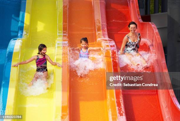 happy family, mother and two girls from 7 and 9 years,  screaming down water slide at water park. - ウォータースライダー ストックフォトと画像