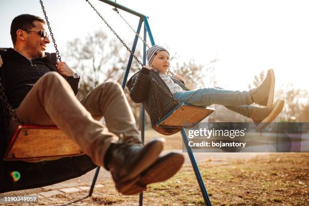 father and son having fun in park - swinging stock pictures, royalty-free photos & images
