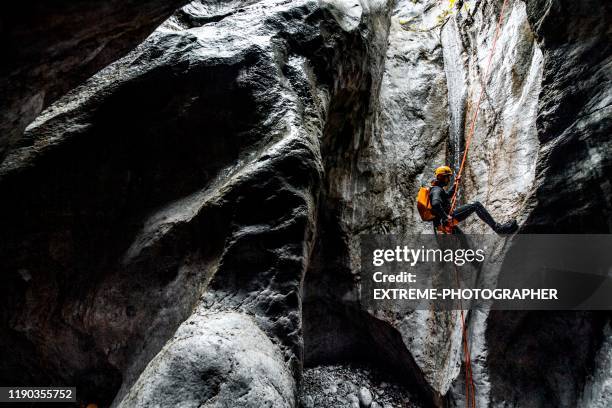 un macho de canyoneering haciendo un abseil por la cuerda estática en una cueva de piedra oscura - garganta fotografías e imágenes de stock