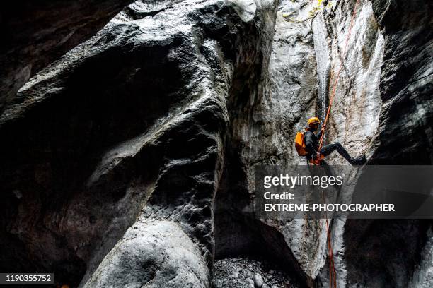 een canyoneering man die een abseil langs het statische touw maakt in een donkere stenen grot - grot stockfoto's en -beelden