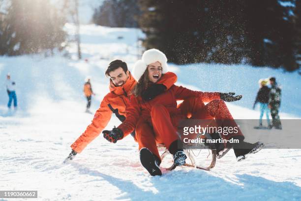 fröhliches paar rodeln im winterurlaub - wintersport stock-fotos und bilder