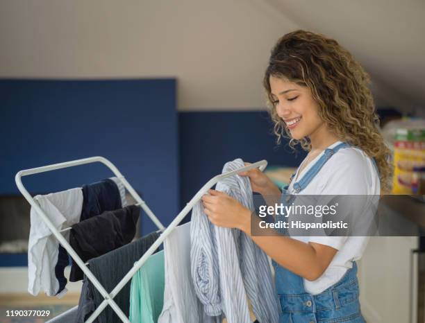 ung kvinna hängande tvätten på torkställ leende hemma - hanging bildbanksfoton och bilder