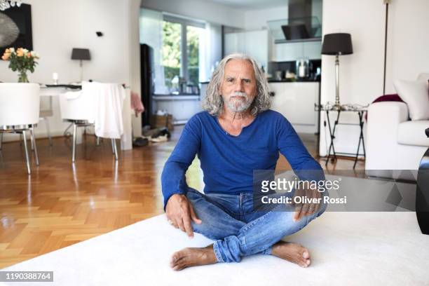 portrait of senior man sitting on the floor at home - con las piernas cruzadas fotografías e imágenes de stock