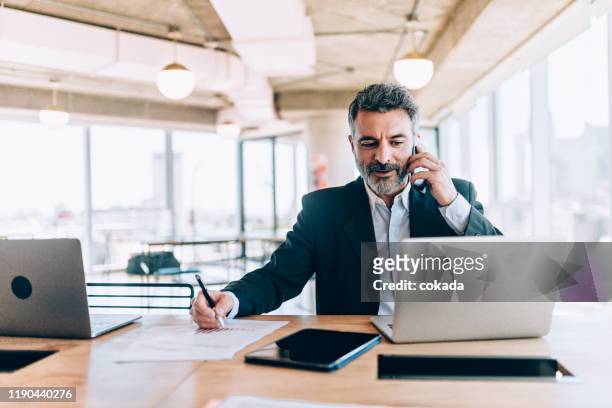 homme d'affaires au bureau parlant sur le téléphone portable - homme d'affaires photos et images de collection