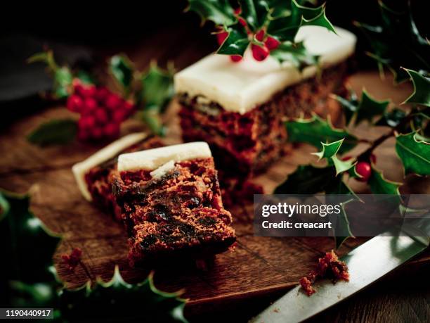 christmas cake on a dark rustic wood surface surrounded by freshly picked holly. - christmas cake stock pictures, royalty-free photos & images