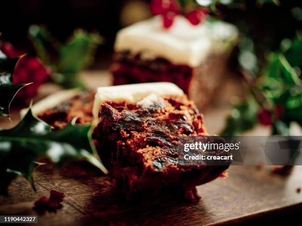 christmas cake on a dark rustic wood surface surrounded by freshly picked holly. - christmas cake stock pictures, royalty-free photos & images