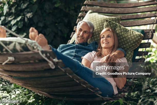 smiling mature couple lying together in a hammock outside - backyard hammock stock pictures, royalty-free photos & images