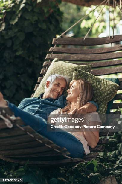 reifes paar lächelnd, während zusammen in einer hängematte draußen liegen - hammock stock-fotos und bilder