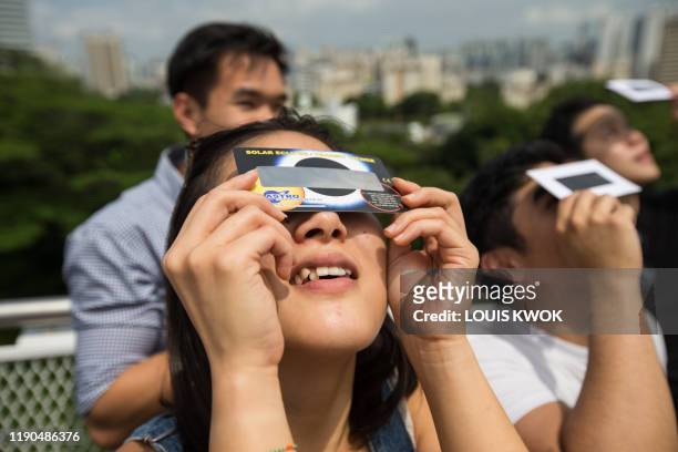 Woman uses a solar filter to watch as the moon moves in front of the sun in a rare "ring of fire" solar eclipse in Singapore on December 26, 2019.