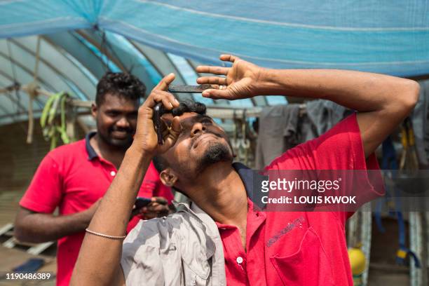 Worker uses a piece of welder's glass to watch as the moon moves in front of the sun in a rare "ring of fire" solar eclipse in Singapore on December...