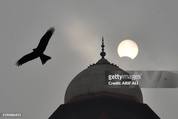 The moon begins to cover the sun during a rare "ring of fire" solar eclipse, while a eagle flies past, at Badshahi mosque in Lahore on December 26,...