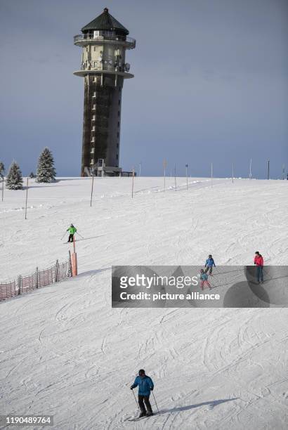 December 2019, Baden-Wuerttemberg, Feldberg Im Schwarzwald: Skiers ski down the slope at the Seebuck in front of the old old SWR_Sendeturm. On the...